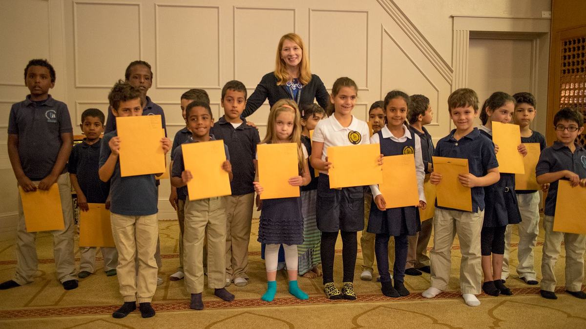 Toledo Islamic Academy students in navy uniforms holding up their certificates, with their teacher standing behind them